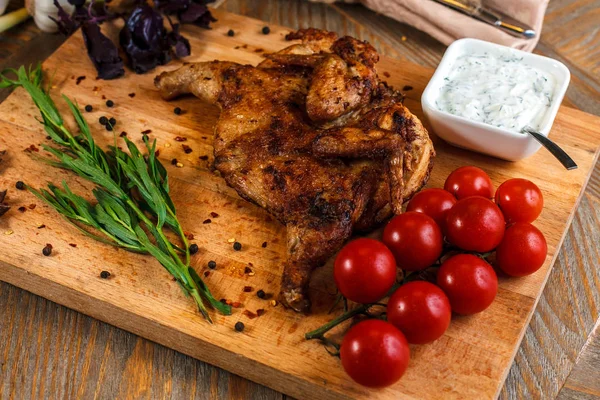 Grilled chicken on a wooden tray with cherry tomatoes and garlic sauce.