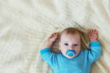 Küçük bir çocuk mavi gömlekli beyaz bir arka plan üzerinde yatıyor.