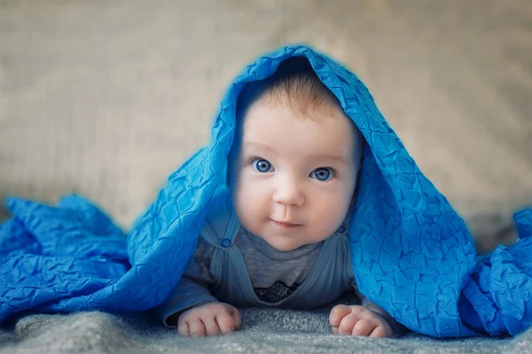 大きな青い目を持つ赤ちゃんは青い布の下からカメラに見える — ストック写真