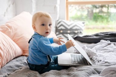 Küçük çocuk büyük bir yatağa oturmuş ve dizüstü kayın kapağını kapatır.