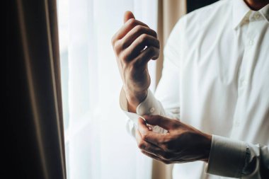 Bir adam bir kol düğmesi ile lüks bir beyaz gömlek kol kol üzerinde takılır. Bir beyaz gömlek ve kol düğmeleri giyen bir adam el kapatın. Damat kol düğmeleri yakalar.