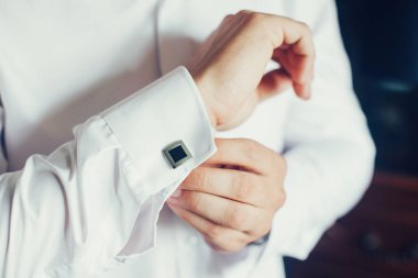 Bir adam bir kol düğmesi ile lüks bir beyaz gömlek kol kol üzerinde takılır. Bir beyaz gömlek ve kol düğmeleri giyen bir adam el kapatın. Damat kol düğmeleri yakalar.