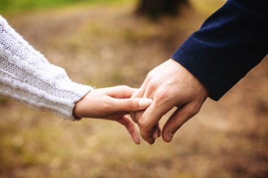 Erkek ve kadın sonbahar ormandaki bir yolda el ele tutuşarak.