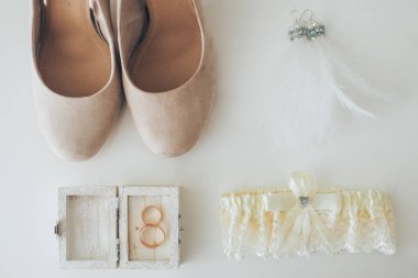 Düğün aksesuar gelin. Şık ayakkabılar, küpe, altın yüzük, beyaz arka plan üzerinde duran jartiyer. düz yatıyordu. üstten görünüm. Evlilik kavramı.