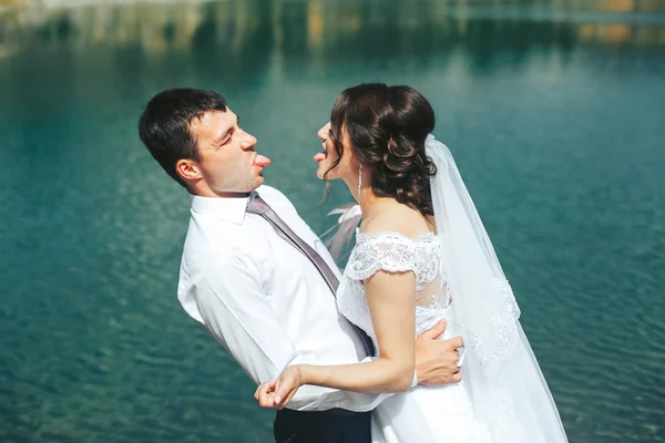 Un beau couple de jeunes mariés debout près d'un lac bleu clair. Amusant — Photo