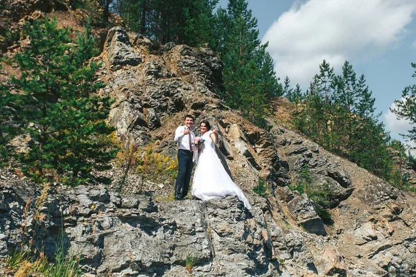 Felices recién casados parados en las rocas cerca del lago azul claro —  Fotos de Stock