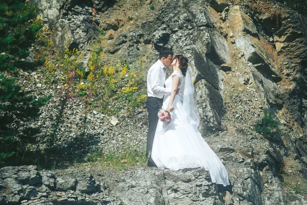 Felices recién casados parados en las rocas cerca del lago azul claro —  Fotos de Stock