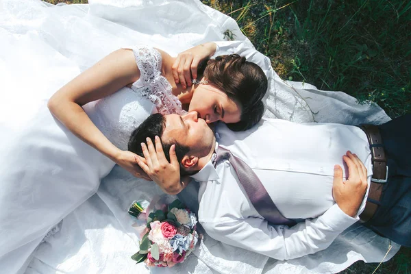 A noiva e o noivo estão em um prado verde e se aquecem ao sol — Fotografia de Stock