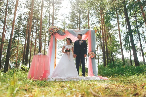 De pasgetrouwden staan in de buurt van de huwelijksboog in het bos — Stockfoto