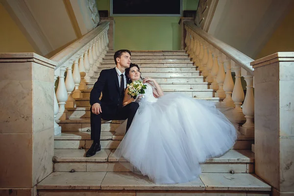 A noiva e o noivo estão sentados em uma escada de mármore branco, hol — Fotografia de Stock