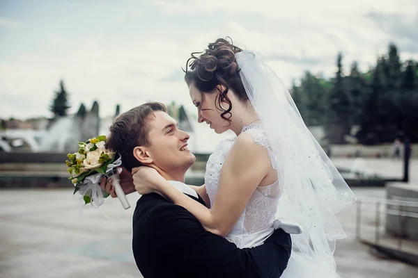 Glücklicher Bräutigam mit einer hübschen Frau in einem weißen Kleid auf dem Rücken — Stockfoto