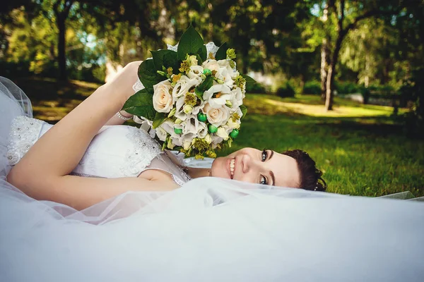 Wunderschöne Braut in einem weißen Kleid auf der grünen Gra liegend — Stockfoto