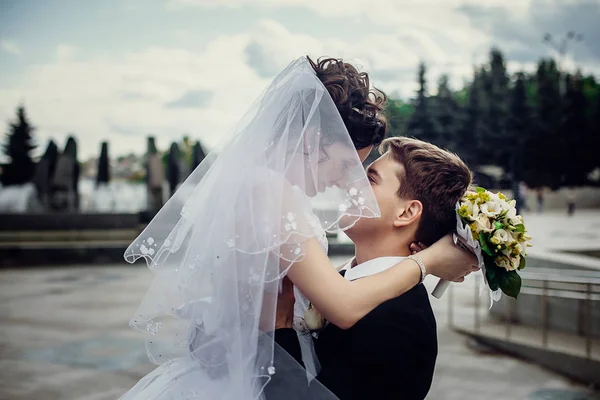 Lycklig brudgum innehav en stilig hustru i en vit klänning på baksidan — Stockfoto