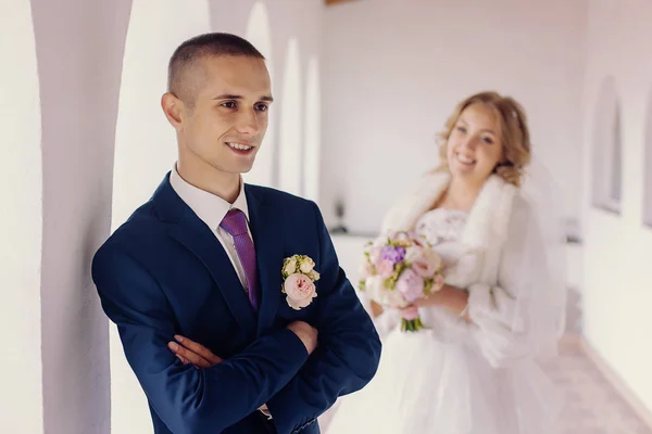 Handsome young man stands in the interior. His bride is standing on a blurred background. — Stock Photo, Image