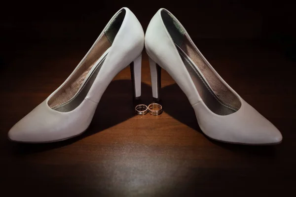 Due anelli d'oro con una scarpa bianca della sposa su sfondo scuro — Foto Stock