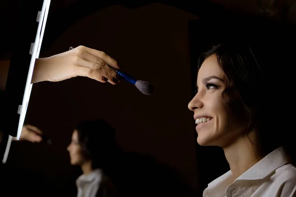 Makeup artist puts makeup on a beautiful brunette girl on a dark background. The concept of beauty