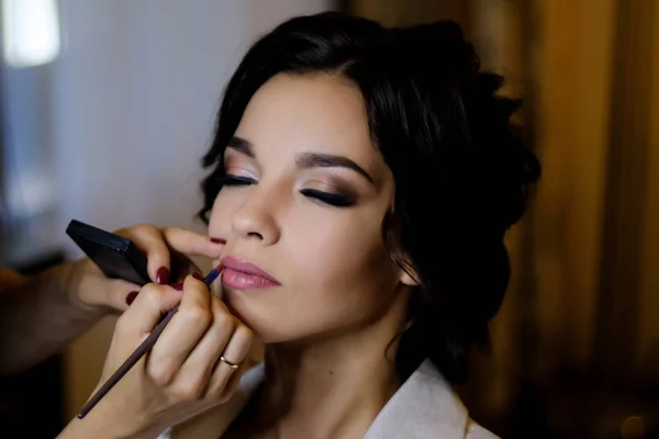 Makeup artist puts makeup on a beautiful brunette girl. The concept of beauty