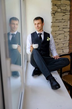 Yakışıklı bir adam büyük bir pencere kenarında oturur ve sabah kahvesini içer