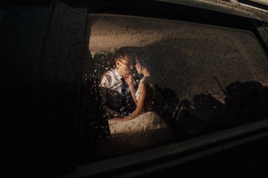 Gelin ve damat öpüşme arabaya geç başı gecelik dışarıda yağmur yağıyor. Gelin ve damat ıslak camın arkasında fotoğrafı