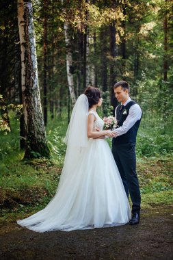 Gelini lüks uzun beyaz elbise ve onu damat poz güzel bir yeşil orman arka planı