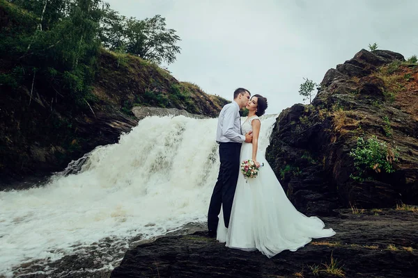Feliz novia y novio de pie en el fondo de la cascada y abrazos —  Fotos de Stock