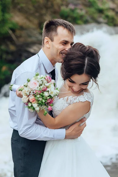 Vackra porträtt av lyckliga bruden och brudgummen i naturen på vattenfall bakgrund — Stockfoto