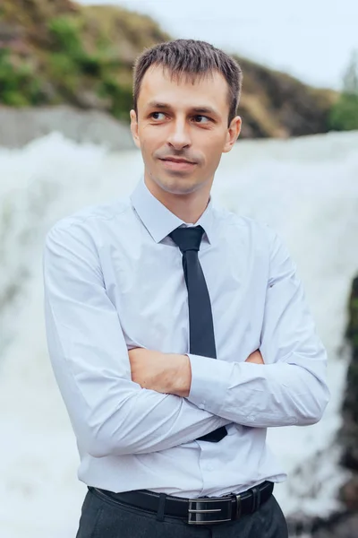 Hermoso retrato de un hombre con camisa y corbata en la naturaleza sobre un fondo de cascada — Foto de Stock