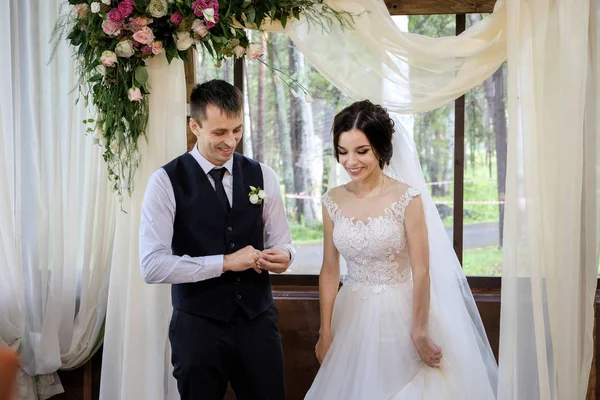 Обмен обручальными кольцами невесты и жениха возле свадебной арки, украшенной цветами — стоковое фото