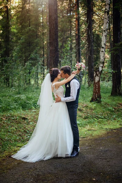 La novia en un lujoso vestido blanco largo y su novio posan sobre el fondo de un hermoso bosque verde —  Fotos de Stock