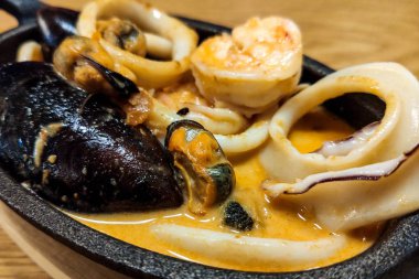 Tahta bir masada, siyah dökme demir bir tavada deniz ürünleri tabağı.