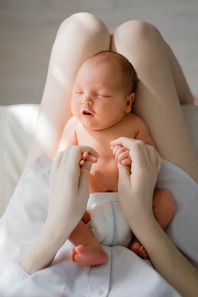 新生児が母親の膝の上に横たわっている。母親は新生児を抱えている。白い寝室でリラックスした女性。家にいる家族 — ストック写真