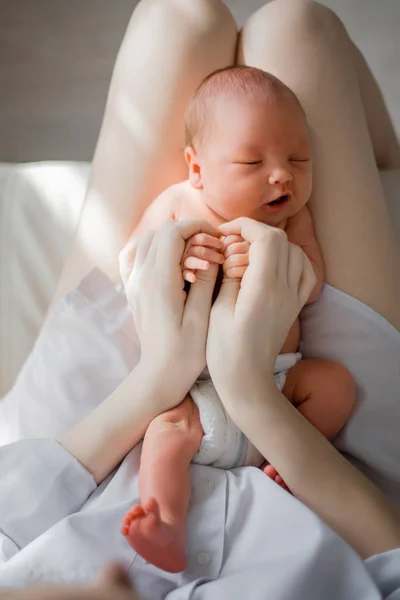 Ett nyfött barn ligger i moderns knä. Mamma håller i sitt nyfödda barn. Kvinnan kopplar av i ett vitt sovrum. Familj hemma — Stockfoto