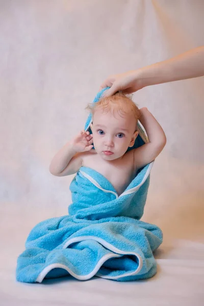 Un niño en una toalla azul sentado sobre un fondo claro después de un baño — Foto de Stock
