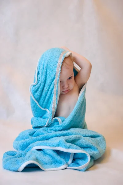 お風呂の後に薄い背景に座っている青いタオルの少年 — ストック写真