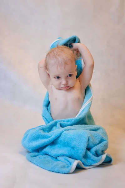 A boy in a blue towel sitting on a light background after a bath — Stock Photo, Image