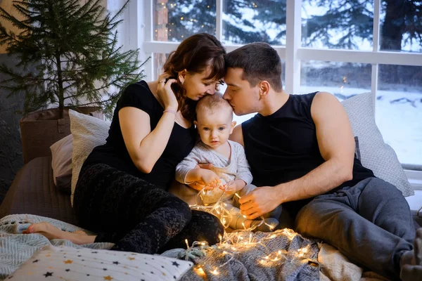 Happy family mom, dad, son are sitting on the bed on Christmas m