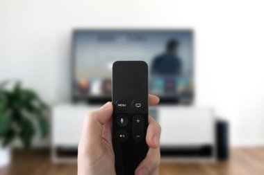Ekrana bakarak ve uzaktan kumanda ile. Bulanık Tv oturma odası arka planda. Multimedya kavramı
