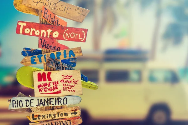 Retro wooden signpost to holiday destination near beach, mini colorful van background. Travel and holiday concept.