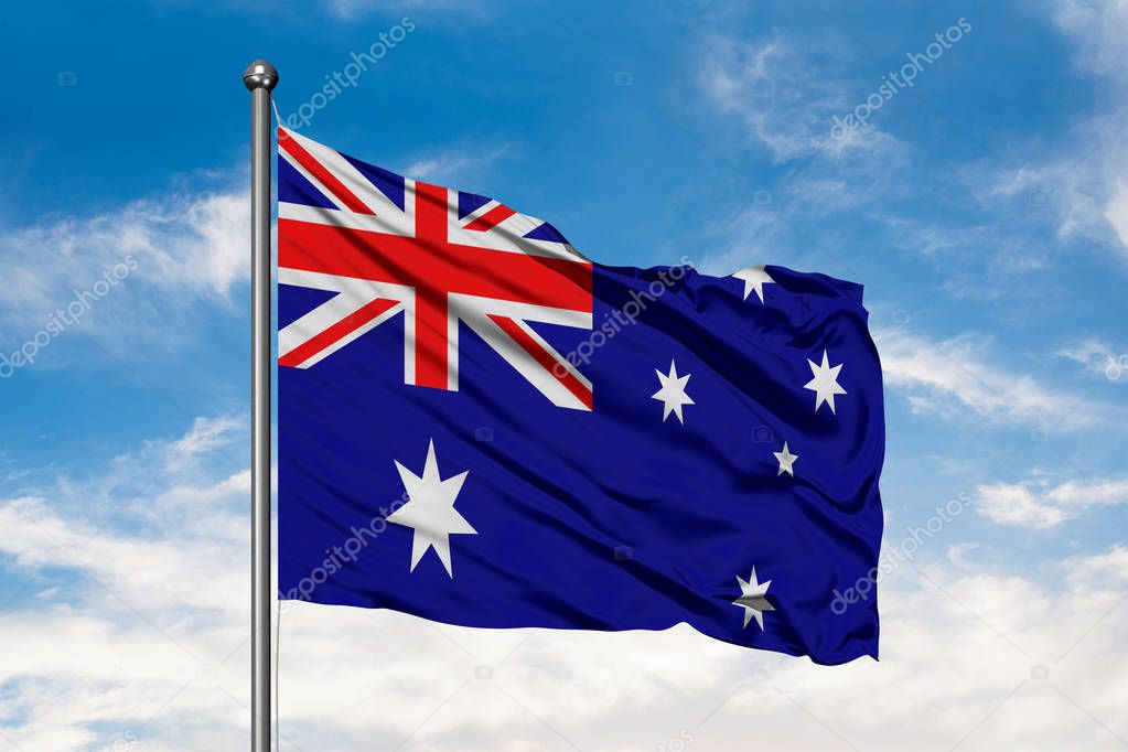 Flag of Australia waving in the wind against white cloudy blue sky. Australian flag.