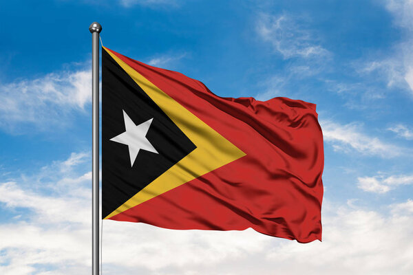 Flag of East Timor waving in the wind against white cloudy blue sky.