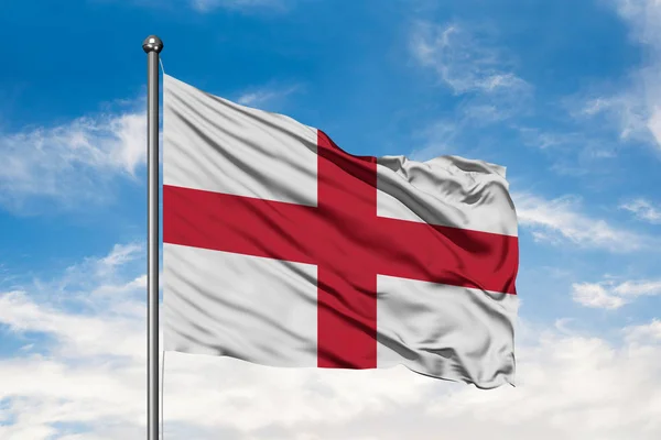 Flag of England waving in the wind against white cloudy blue sky. English flag.