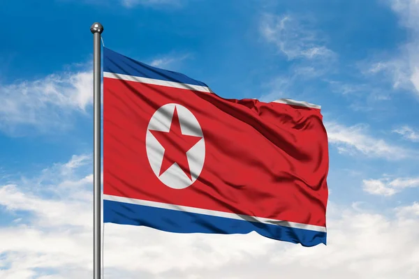 Flag of North Korea waving in the wind against white cloudy blue sky. North Korean flag.