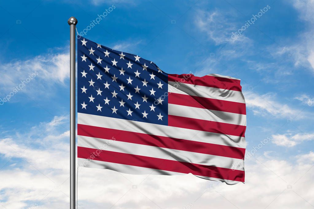 Flag of United States of America waving in the wind against white cloudy blue sky. USA flag.