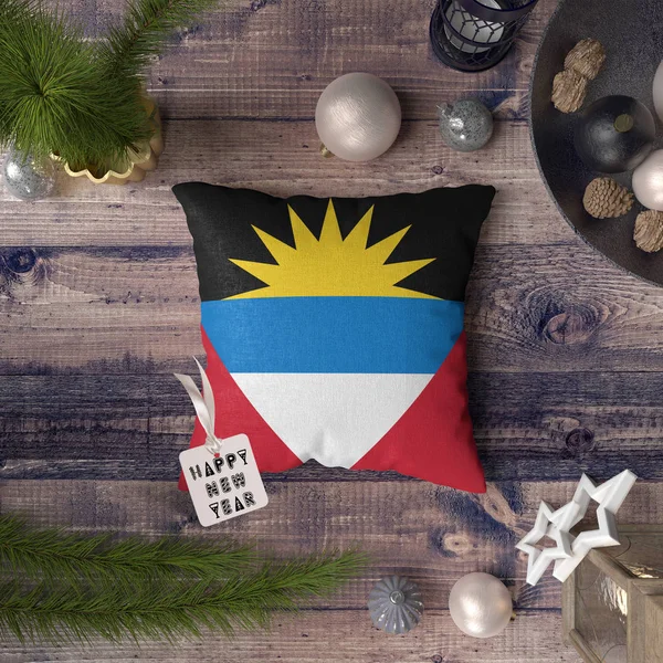 Happy New Year tag with Antigua and Barbuda flag on pillow. Christmas decoration concept on wooden table with lovely objects.