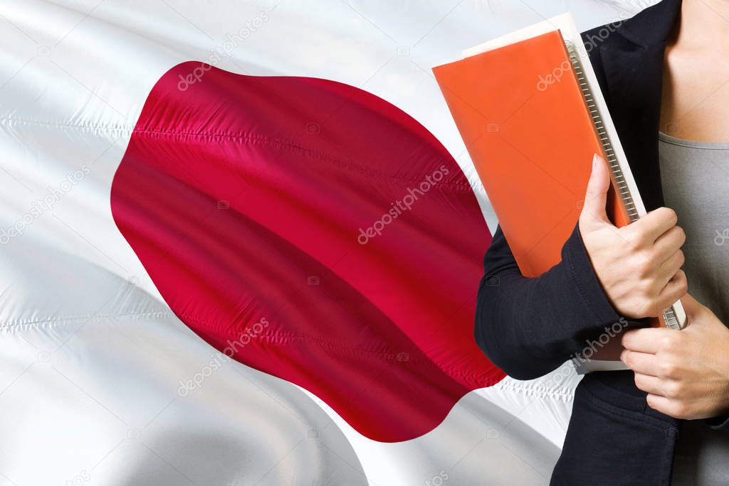 Learning Japanese language concept. Young woman standing with the Japan flag in the background. Teacher holding books, orange blank book cover.