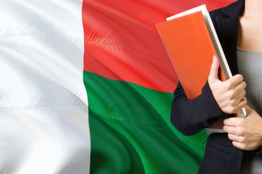 Madagaskar dil kavram öğrenme. Madagaskar bayrağı arka planda duran genç kadın. Kitaplar, turuncu boş kitap kapağı tutan öğretmen.