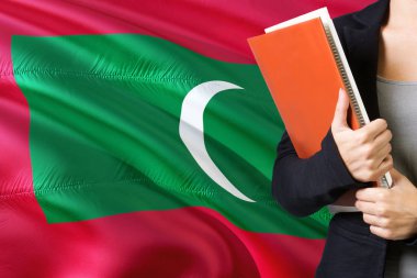 Öğrenme Maldivan dil kavram. Maldivler bayrağının arka planda duran genç kadın. Kitaplar, turuncu boş kitap kapağı tutan öğretmen.