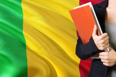 Malili dil kavram öğrenme. İçinde belgili tanımlık geçmiş Mali bayrağı ile duran genç kadın. Kitaplar, turuncu boş kitap kapağı tutan öğretmen.