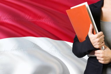 Monakolu dil kavram öğrenme. Monaco bayrağı arka planda duran genç kadın. Kitaplar, turuncu boş kitap kapağı tutan öğretmen.