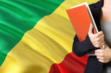 Kongolu dil kavram öğrenme. Kongo Cumhuriyeti bayrağı arka planda duran genç kadın. Kitaplar, turuncu boş kitap kapağı tutan öğretmen.